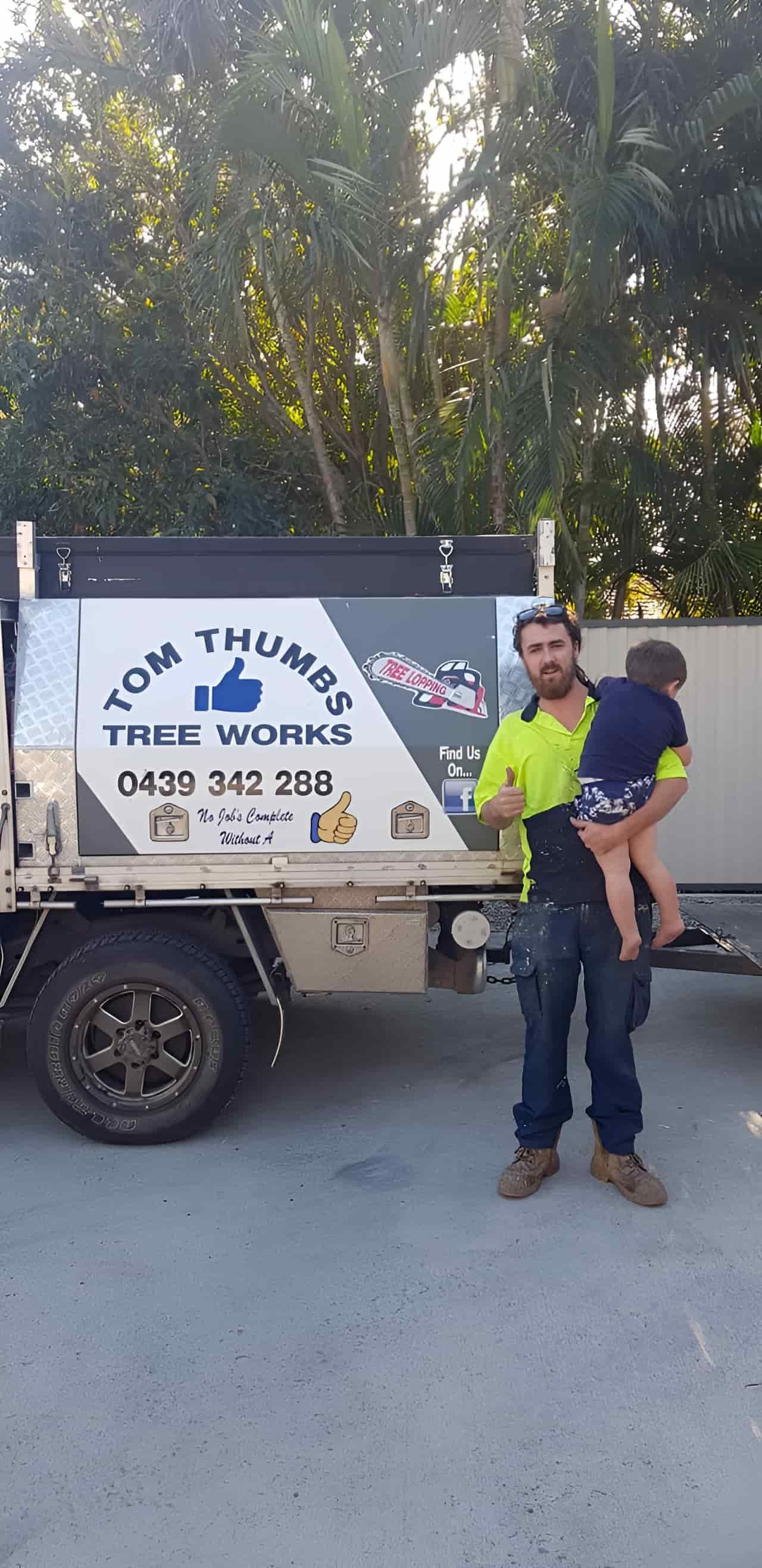 A Man Is Holding A Child On His Shoulders In Front Of A Truck — Tom Thumbs Tree Works In Beachmere, QLD