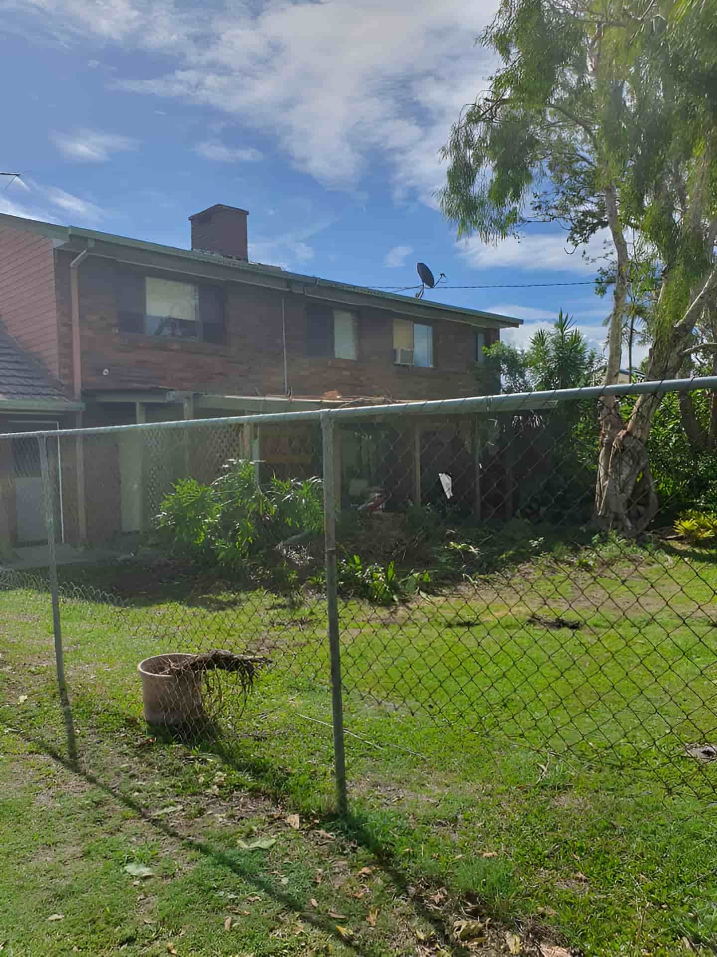 A Chain Link Fence Surrounds A Lush Green Yard In Front Of A Brick House — Tom Thumbs Tree Works In Delaneys Creek, QLD