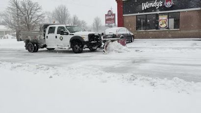 White tow truck in snowy parking lot near a Wendy’s, clearing snow from a car in winter weather