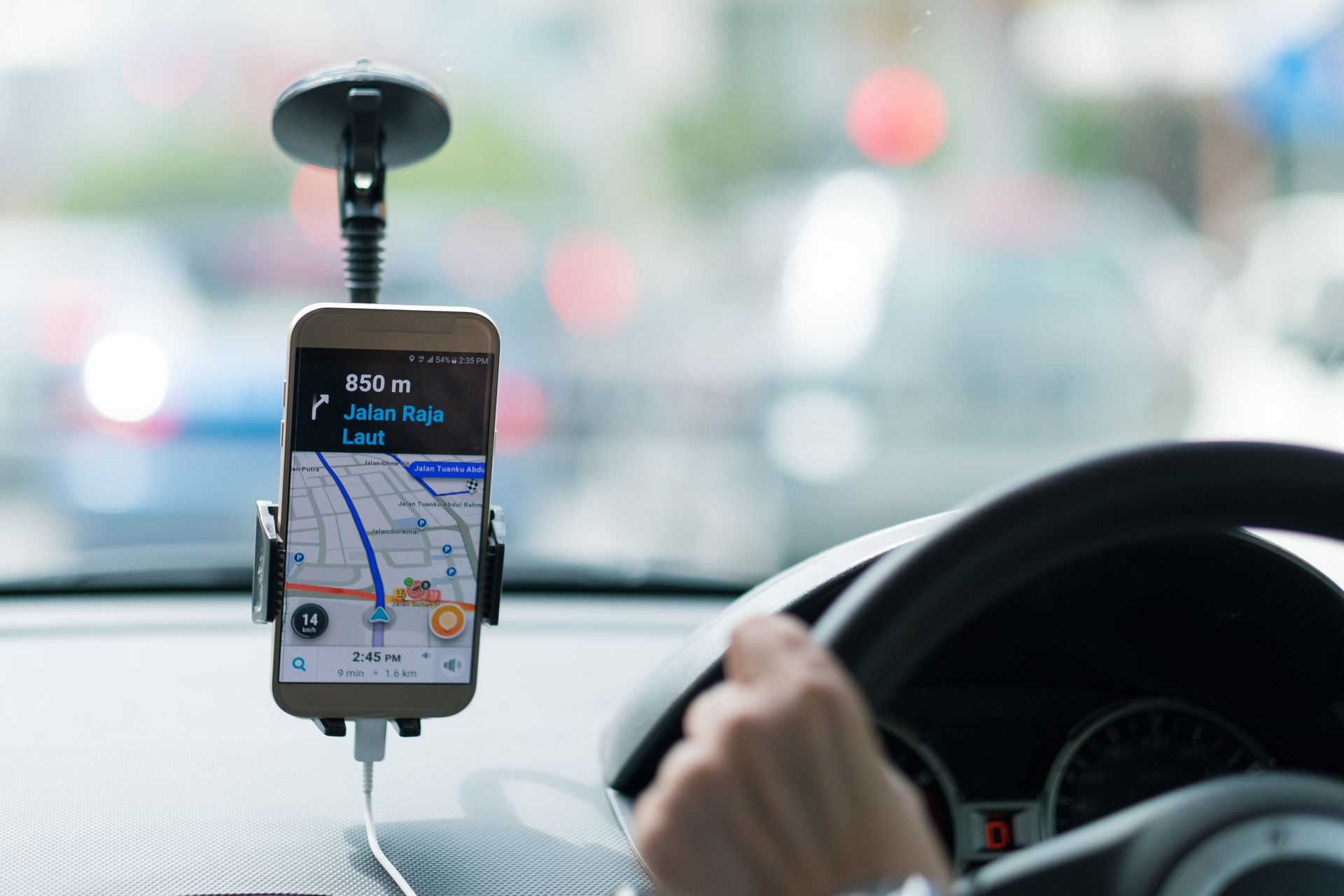 A person is driving a car with a cell phone on the dashboard.