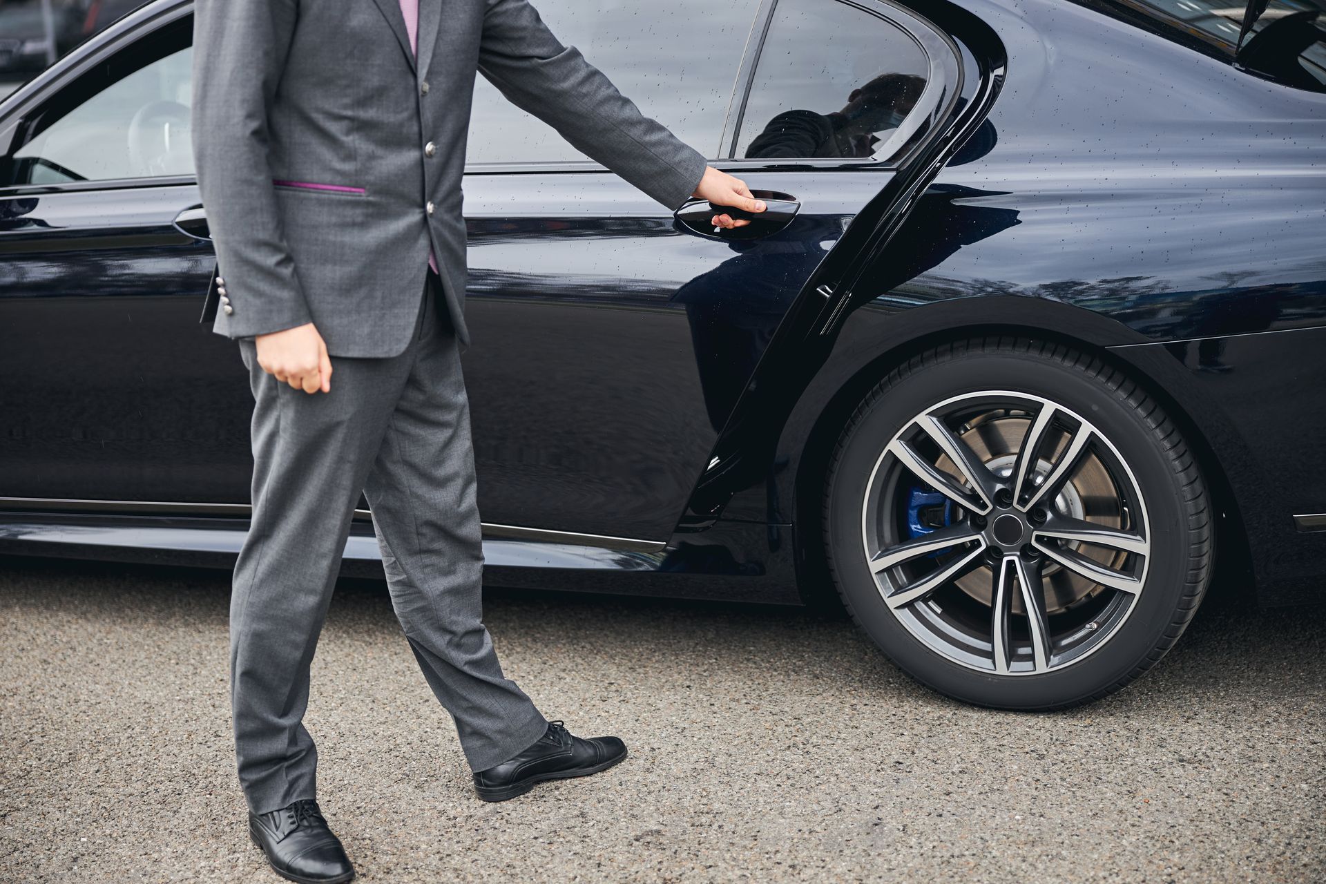 A man in a suit is opening the door of a black car.