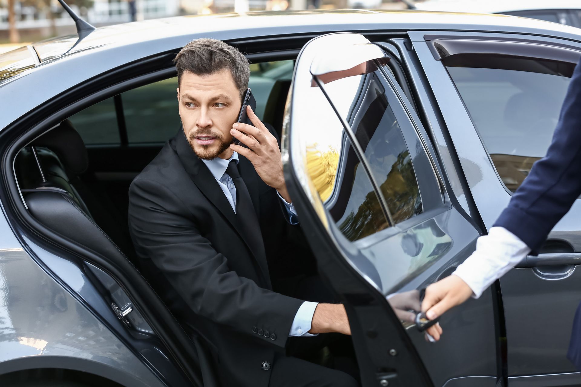 A man in a suit is getting out of a car while talking on a cell phone.