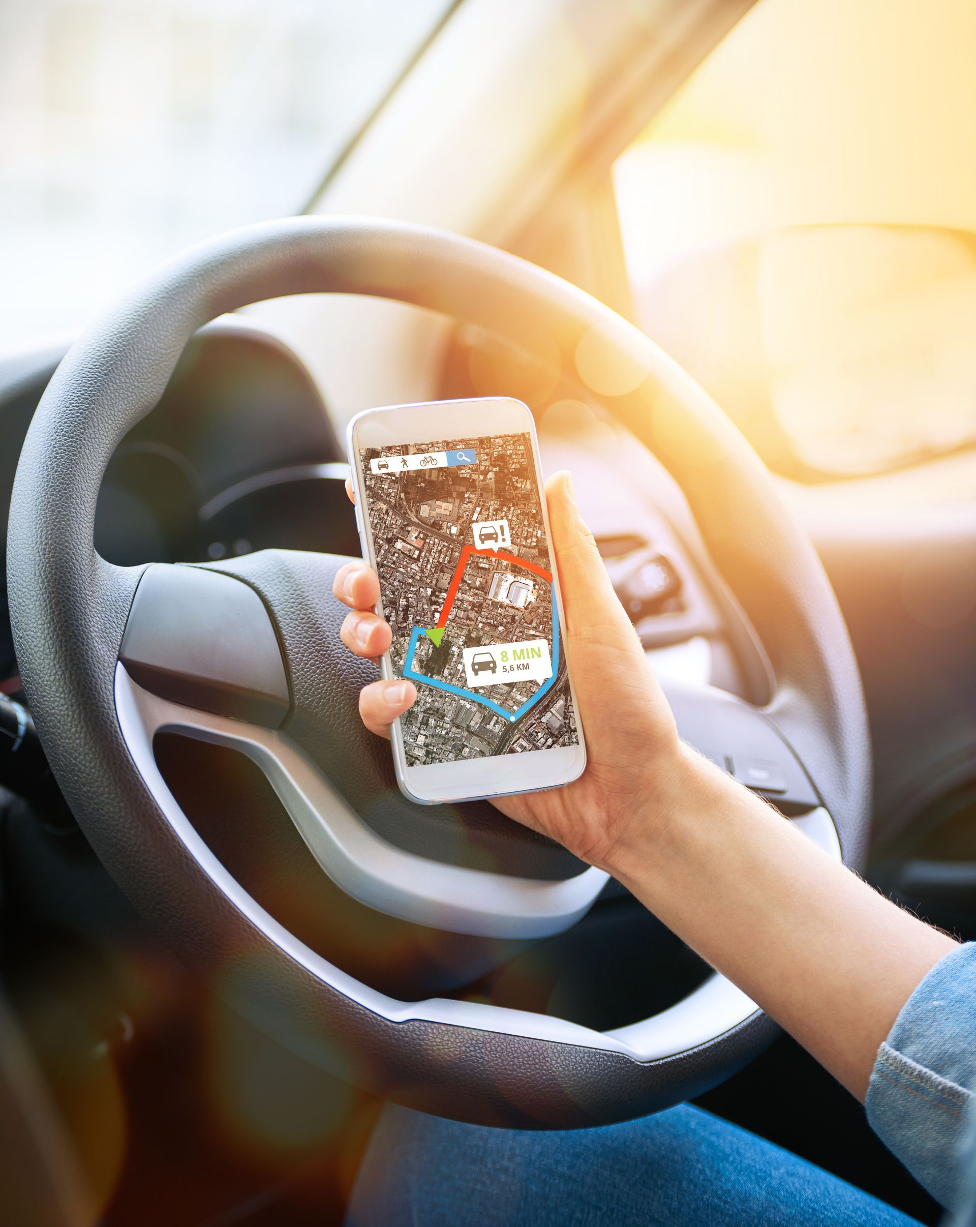 A person is holding a cell phone in their hand while driving a car.