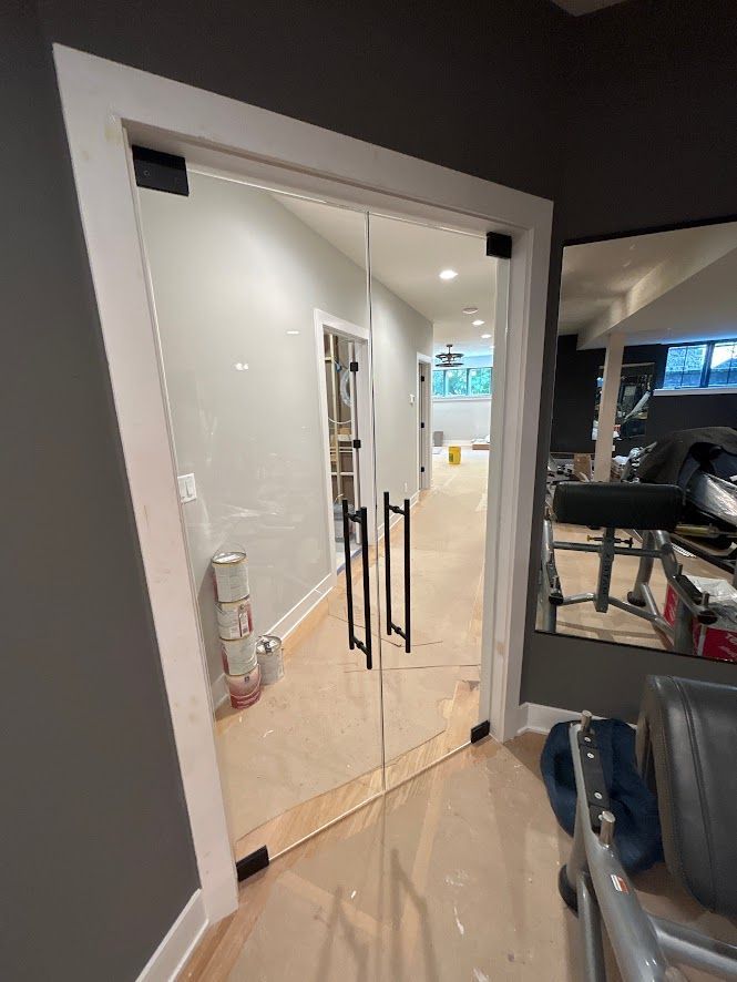 Glass double doors with black handles, set in a white frame, lead into a hallway.