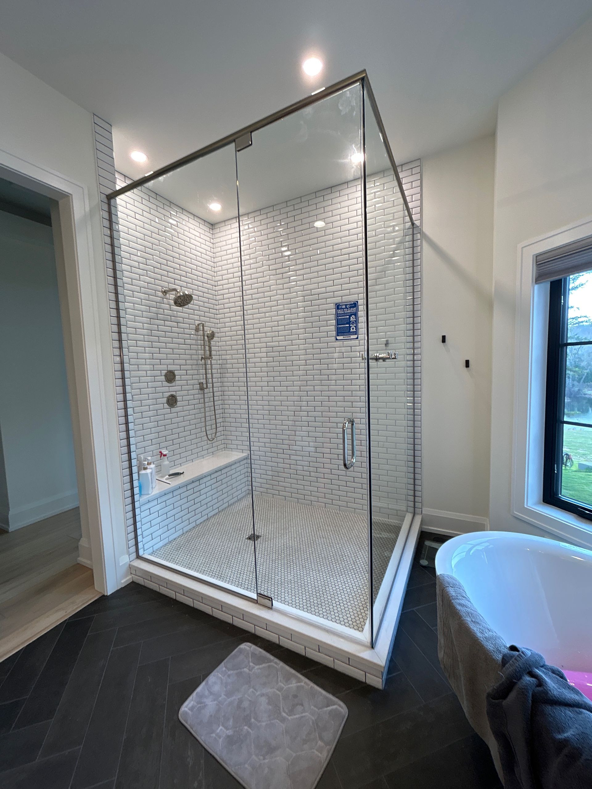 Modern bathroom with glass shower, patterned white tile walls, dark floor, and a freestanding tub.