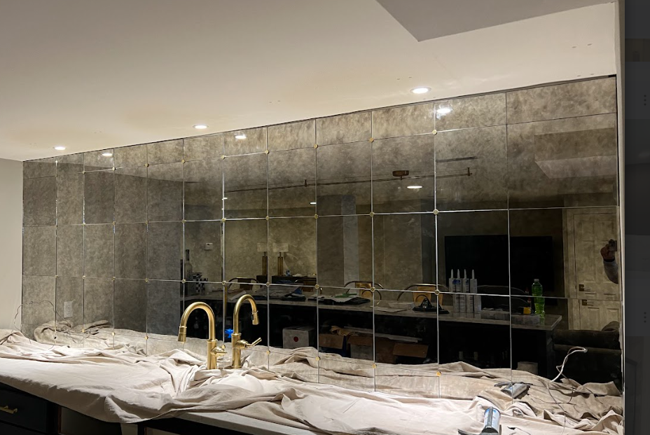 A kitchen with a mirrored backsplash, gold faucets, and a stone countertop covered with protective cloth.