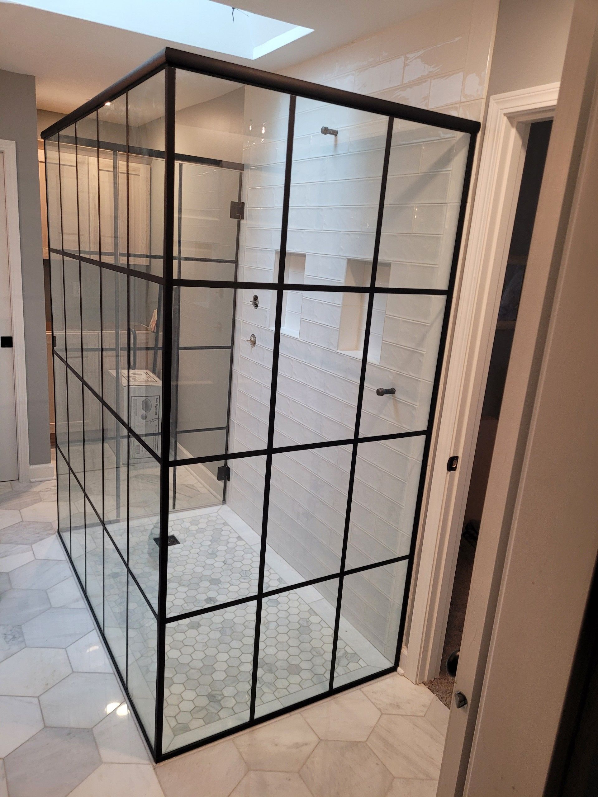 Modern glass shower enclosure with black grid frame, hexagon tile floor, and white walls.