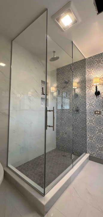 Corner shower with glass doors, black trim, and marble tile walls, beside a white vanity.