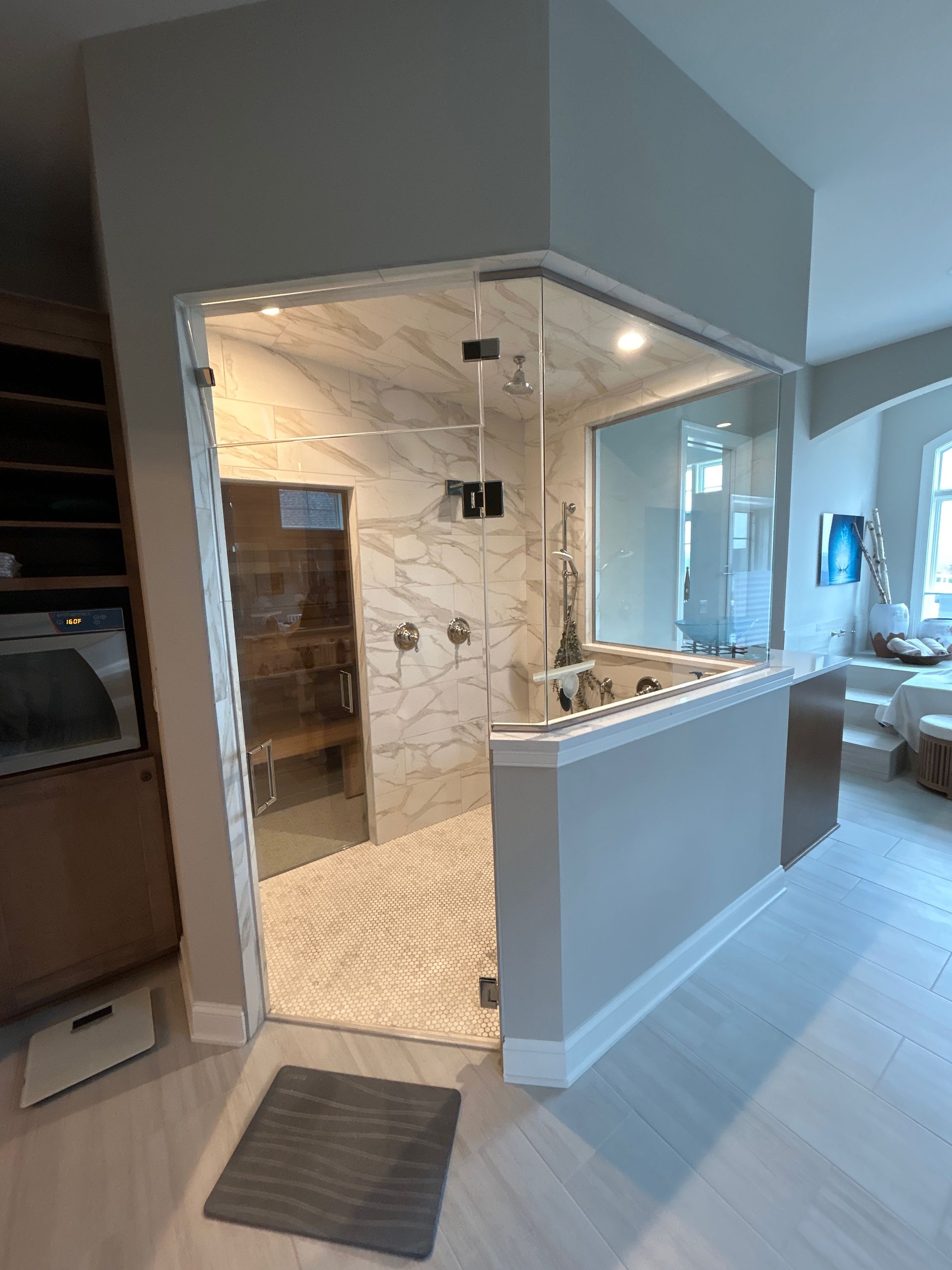 Modern bathroom with glass shower enclosure, marble tile, and white floor, built-in bench.