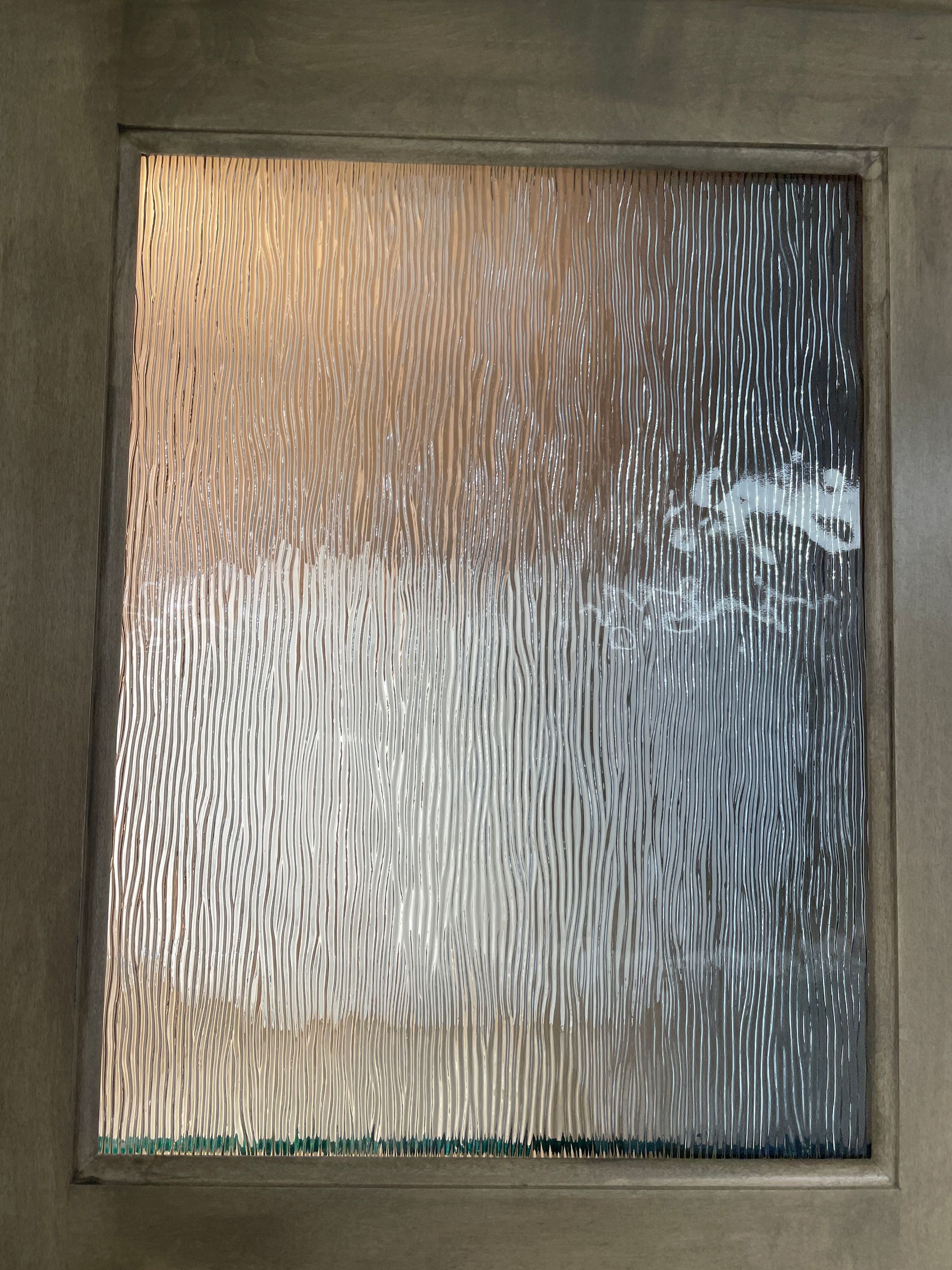 Frosted glass panel in a brown wooden door frame, textured with vertical lines and organic patterns.