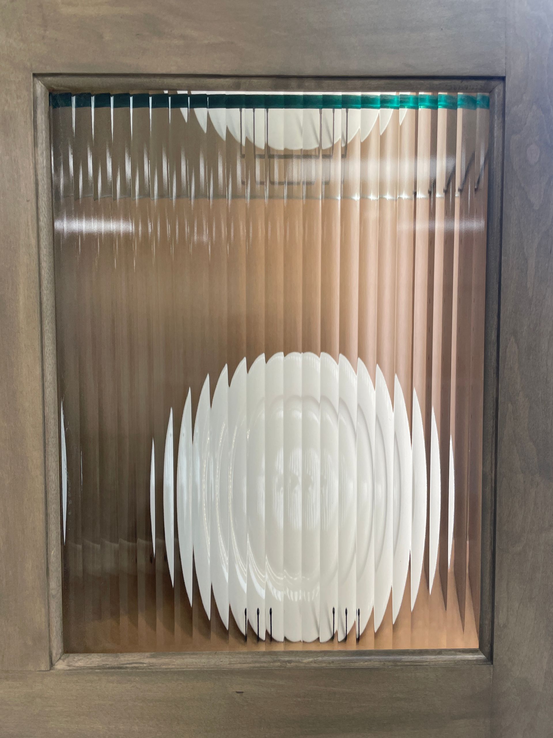 White plates viewed through textured glass pane in a wooden frame.