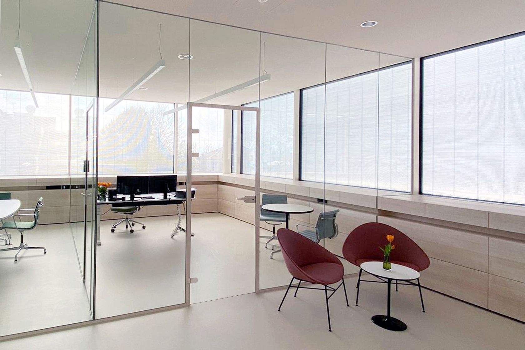 Modern office space with glass walls, multiple workstations, and lounge area with chairs.