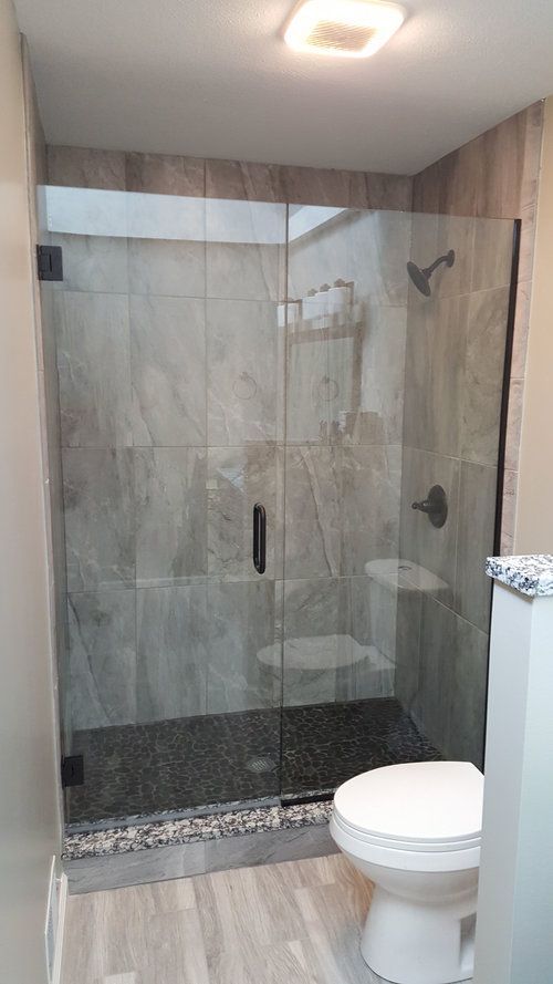 Modern shower with glass doors, stone tile, dark hardware, and a toilet.