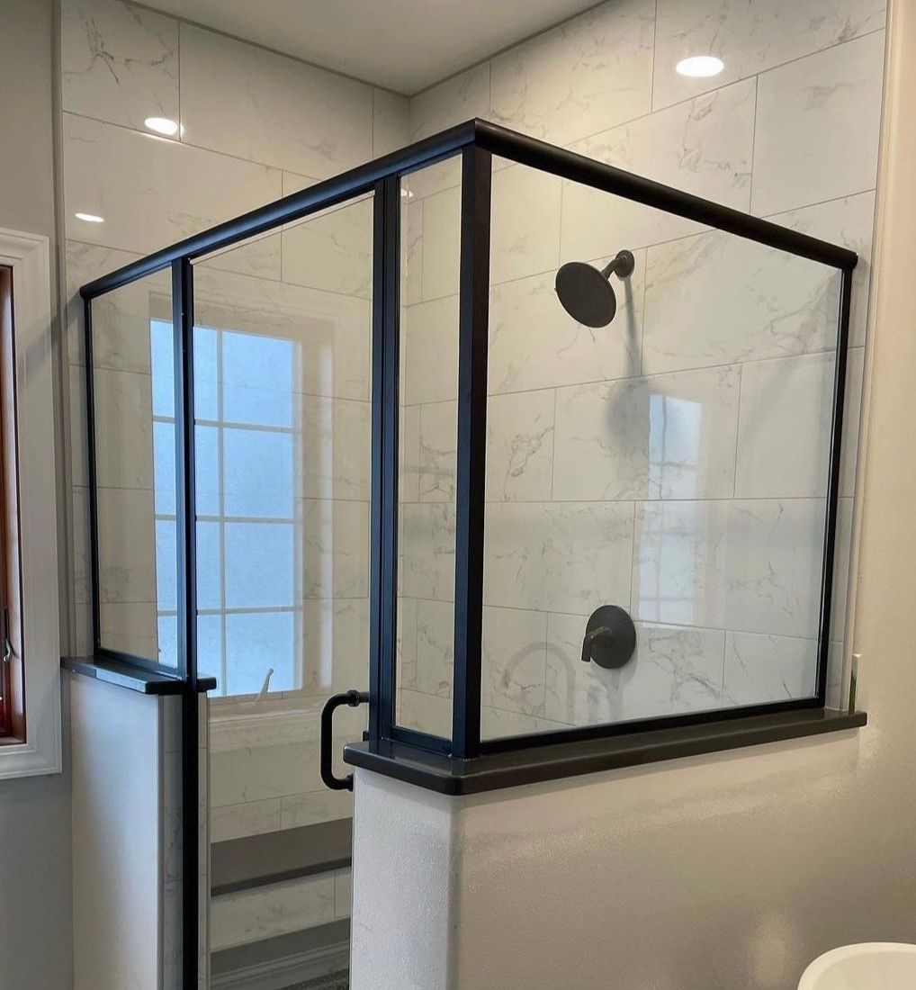 Black-framed glass shower enclosure with dark fixtures and light-colored tile walls.