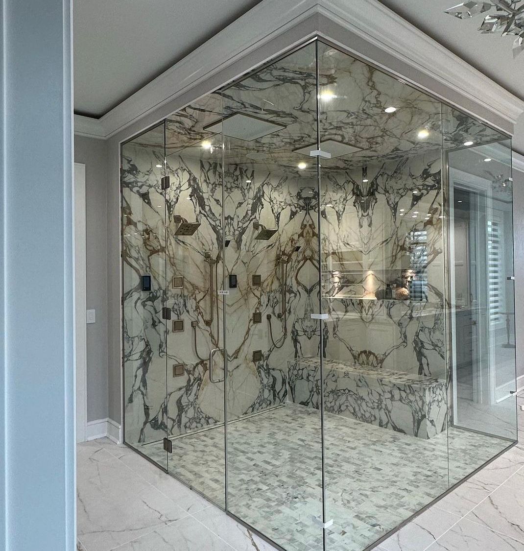 Glass-enclosed shower with marble walls and ceiling.  Gray and white marble, glass doors, and recessed lighting.