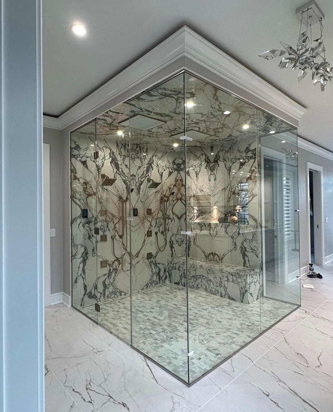 A bathroom with marble walls and a walk in shower with glass doors.