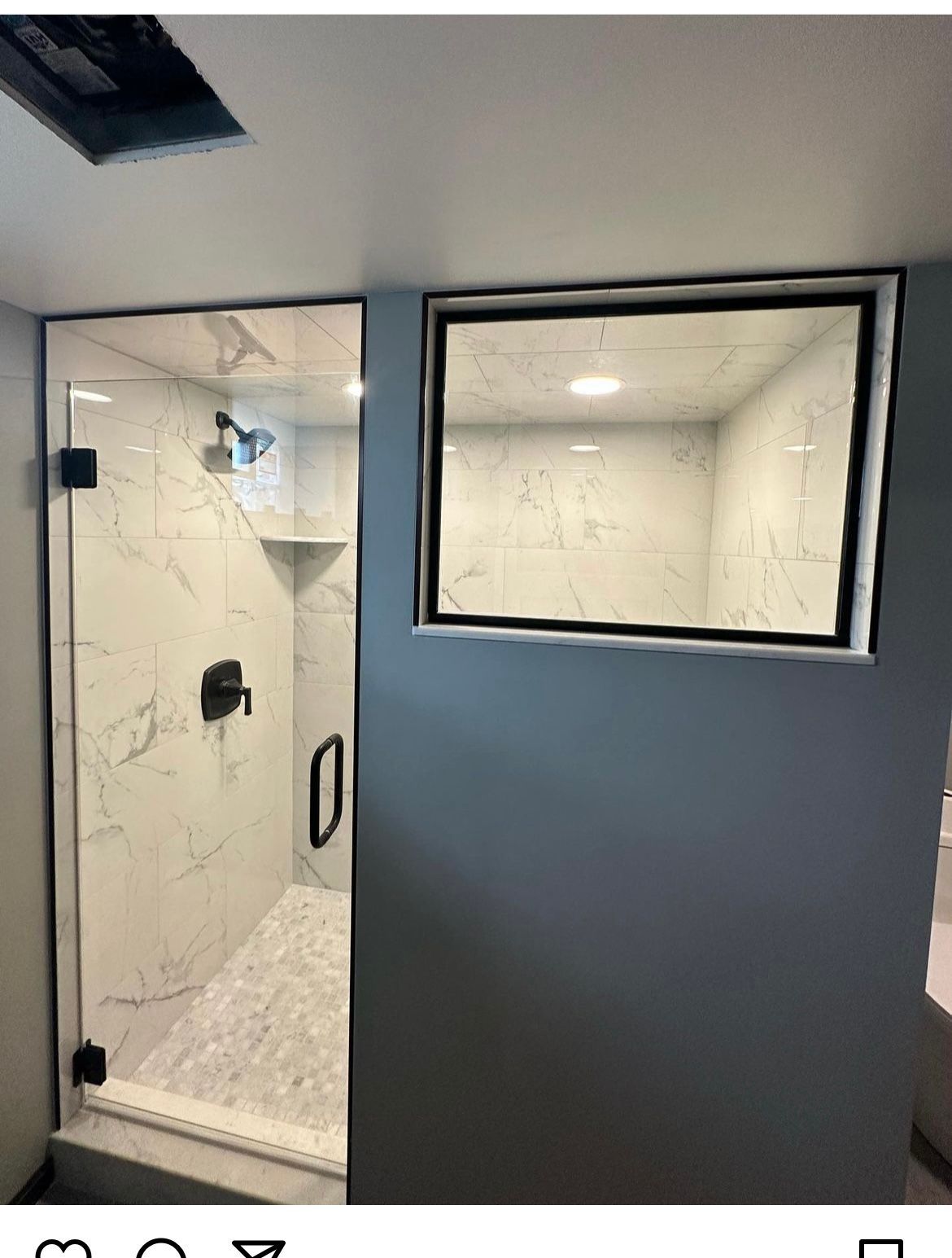 Shower stall with glass door, black fixtures, and marble-like tile. Adjacent is a window with black trim.