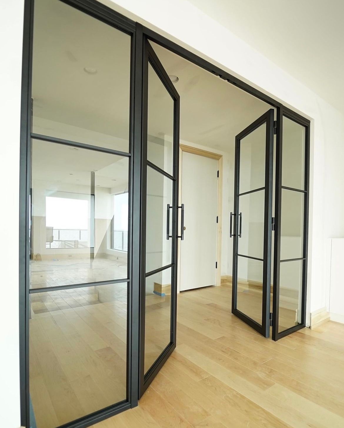 Black framed glass doors open to reveal an interior space with hardwood floors.
