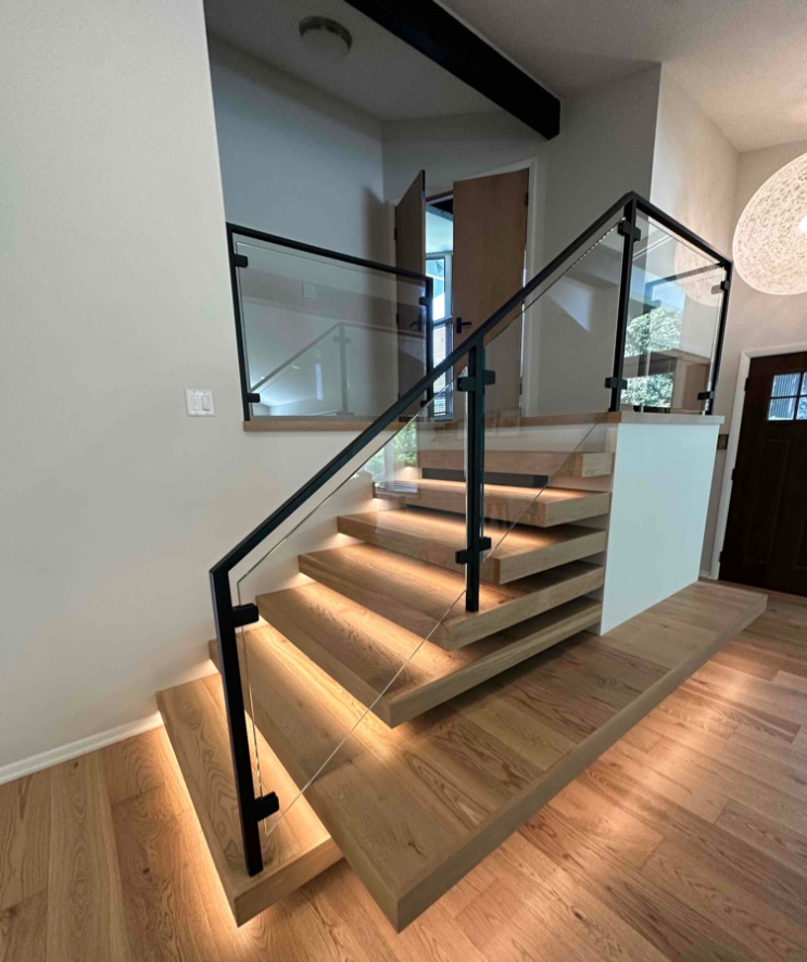 Modern wooden staircase with glass railing and under-step lighting.