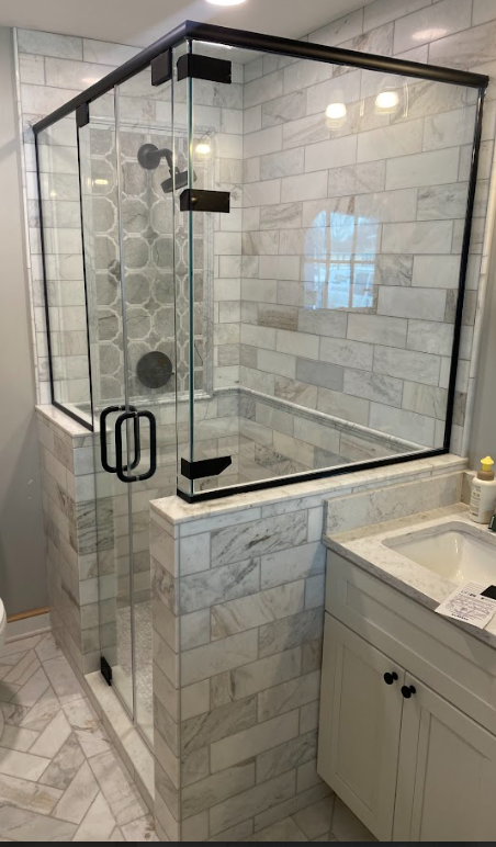 Corner shower with glass doors, white marble tiles, black hardware, and a small vanity.