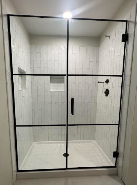 Black-framed glass shower enclosure with white tile walls and a white shower base in a bathroom.