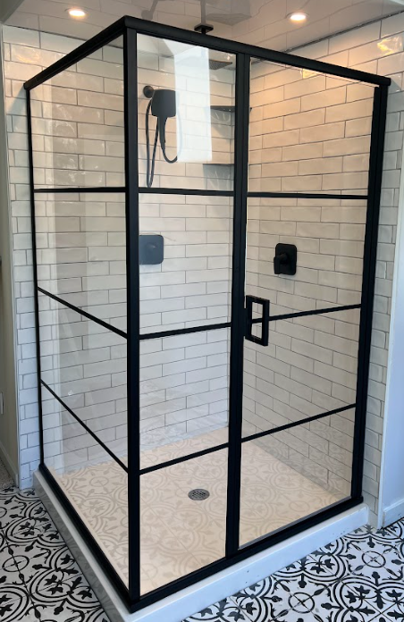 Black-framed glass shower enclosure with subway tile walls and patterned floor.