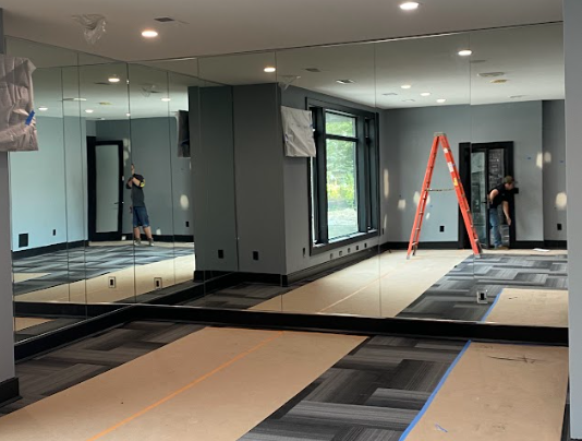 Room with mirrored walls, a large window, and workers installing flooring; a ladder leans against a wall.