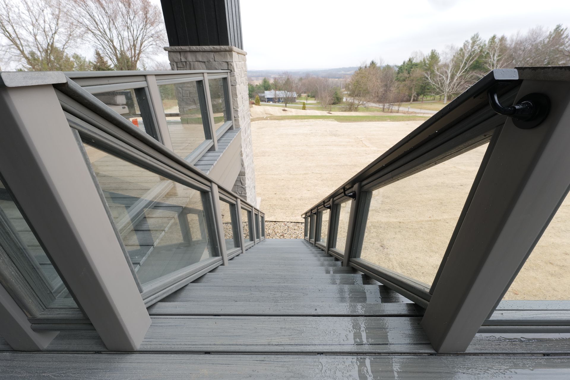 Staircase with glass railings descends to a grassy area, overcast sky visible.