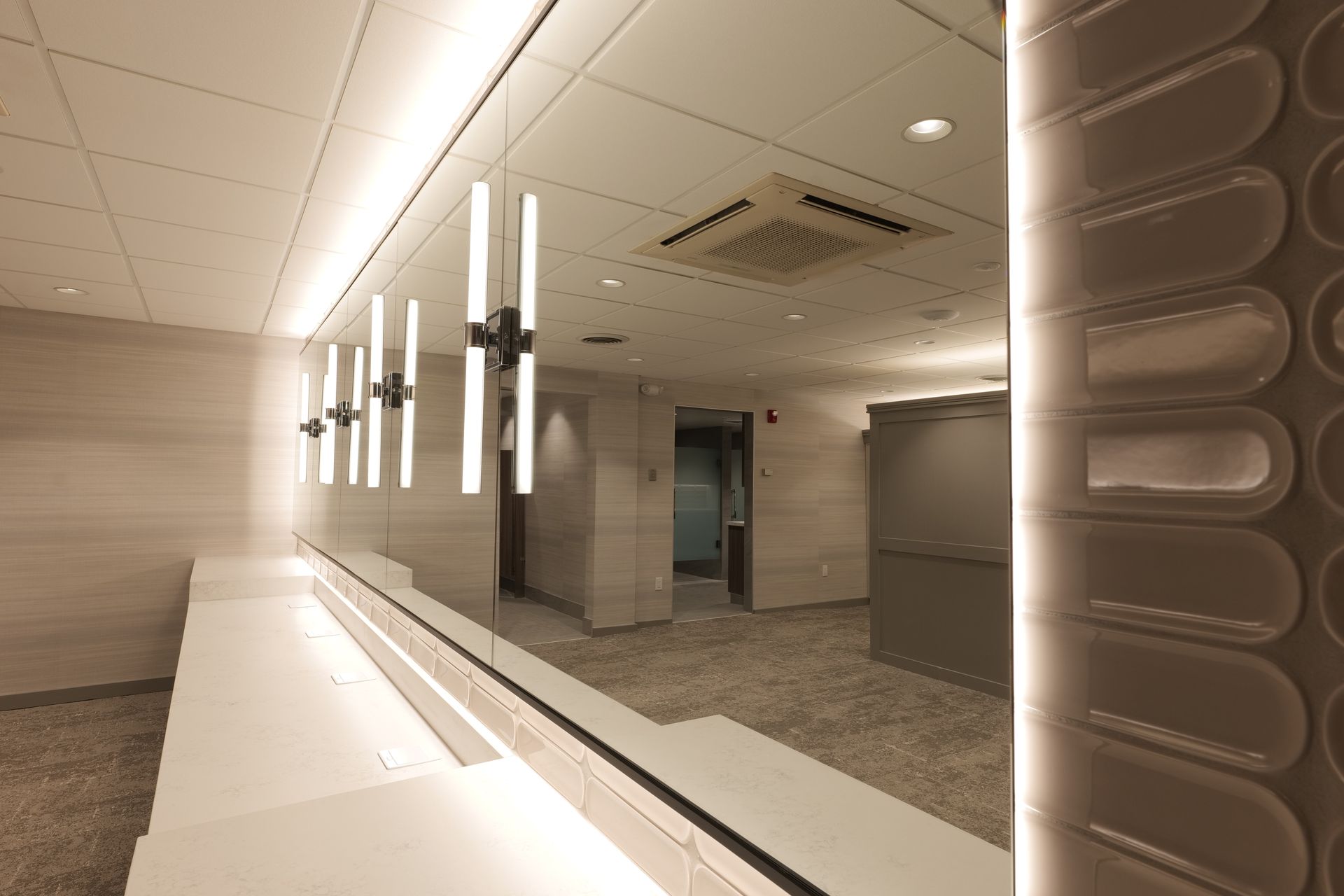 A modern, clean bathroom with a long mirror reflecting the space.  White and beige tones, vertical light fixtures.