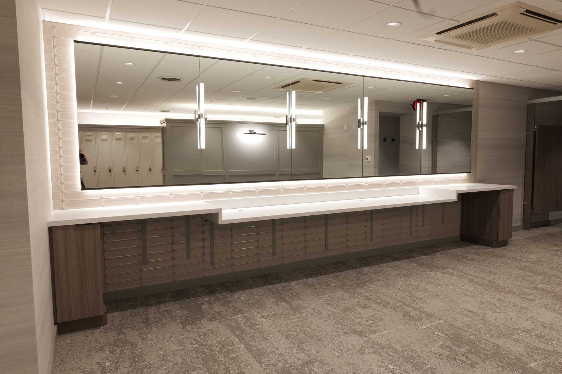 Long countertop with mirror and overhead lights in a modern lobby.