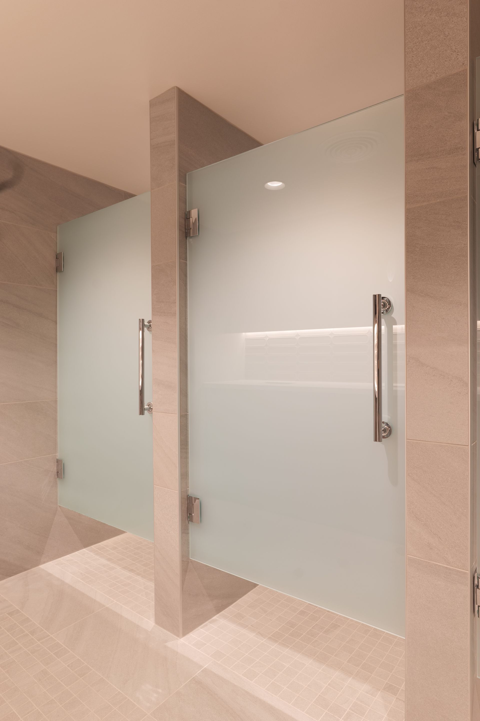 Two frosted glass shower doors in a beige tiled bathroom. Silver handles and hinges.