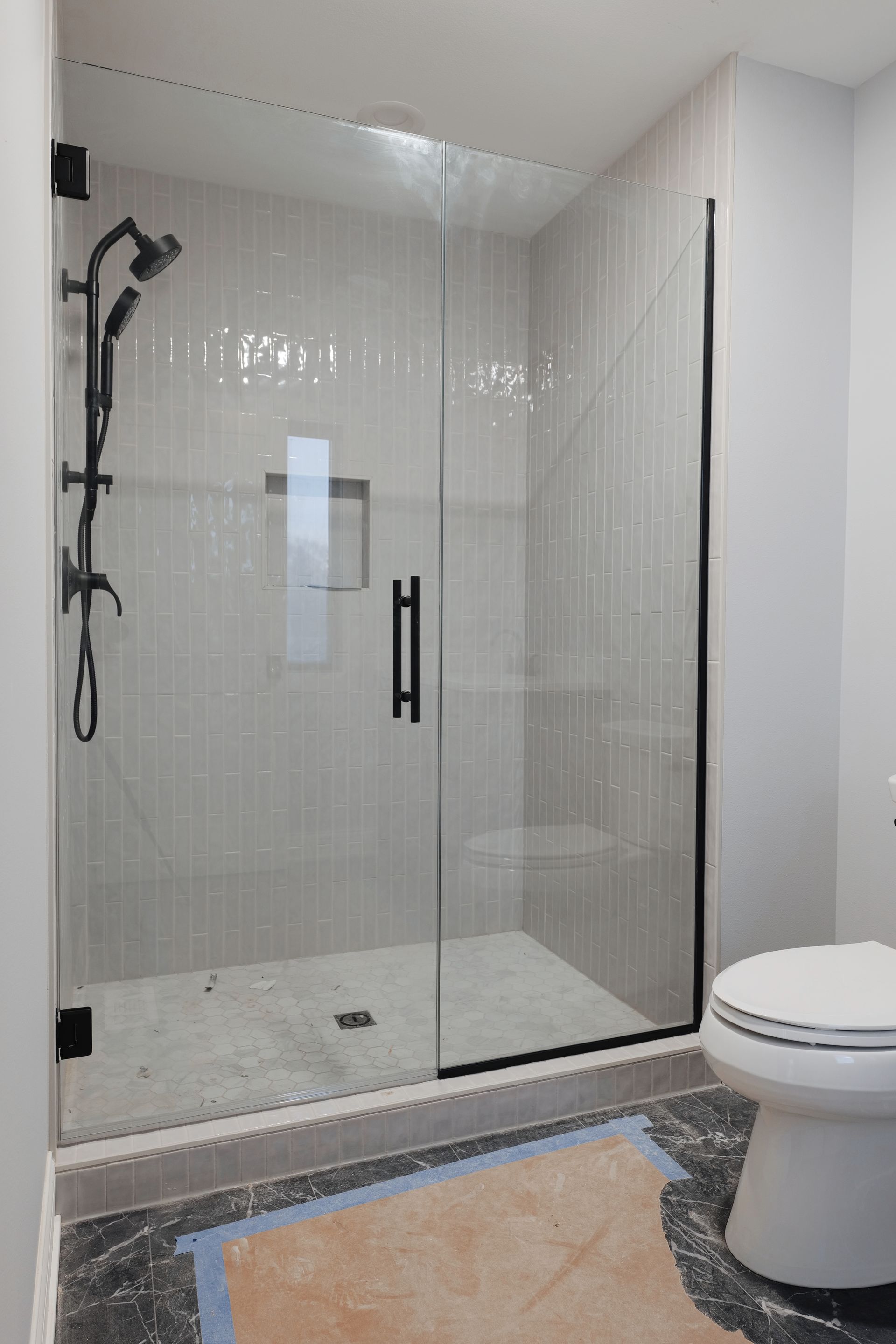 Corner shower with glass doors, black trim, and marble tile walls, beside a white vanity.