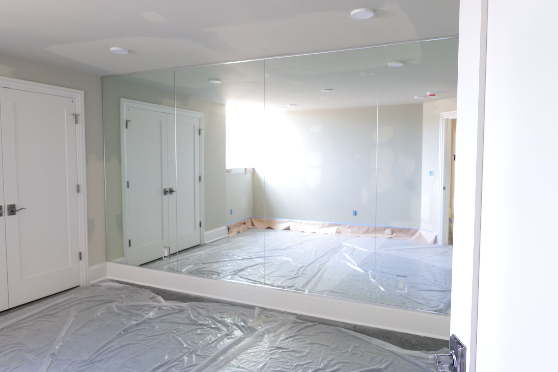 Large mirror on a wall in a room with white doors, light-colored walls, and protective sheeting on the floor.