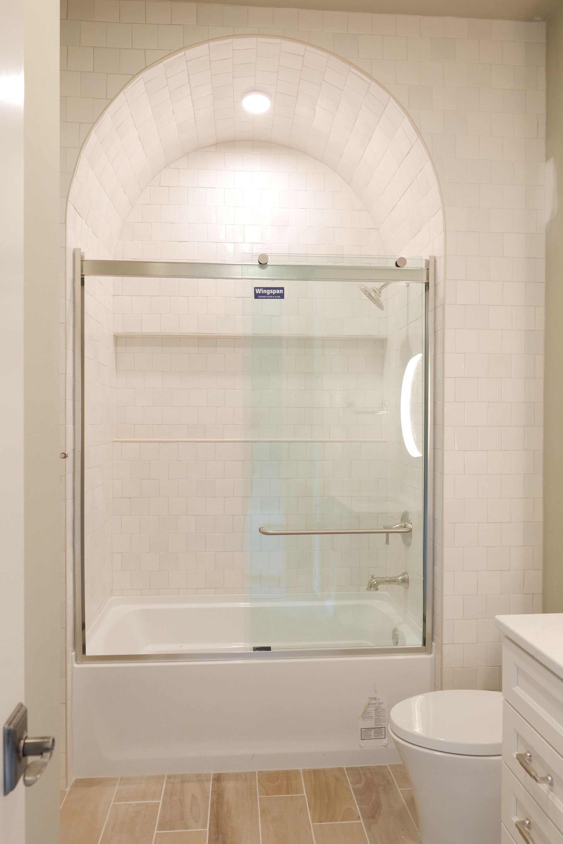 Bathroom with white tile walls and an arched shower enclosure above a bathtub.