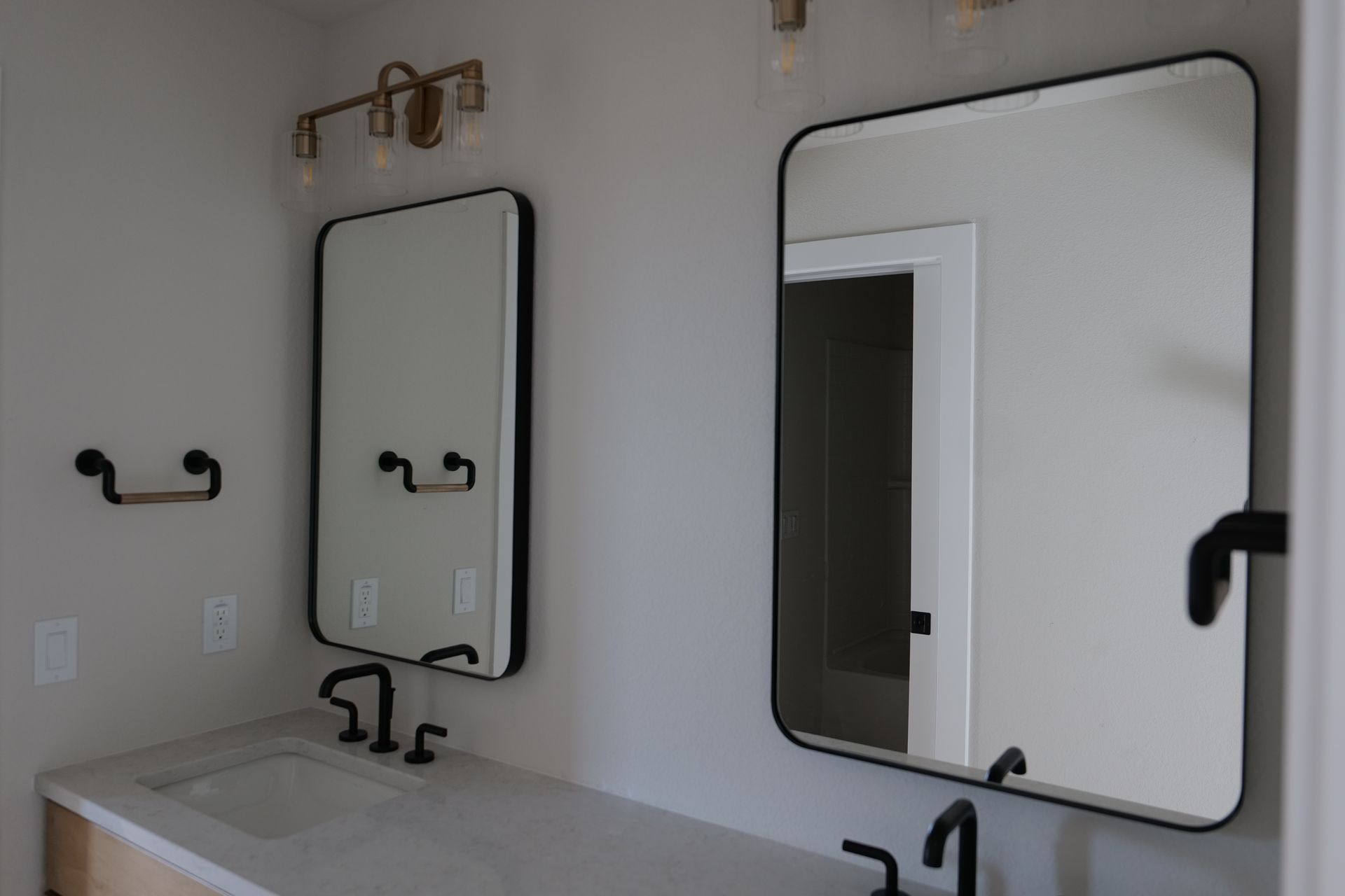 Bathroom with two black-framed mirrors, vanity with a sink, and gold light fixtures.