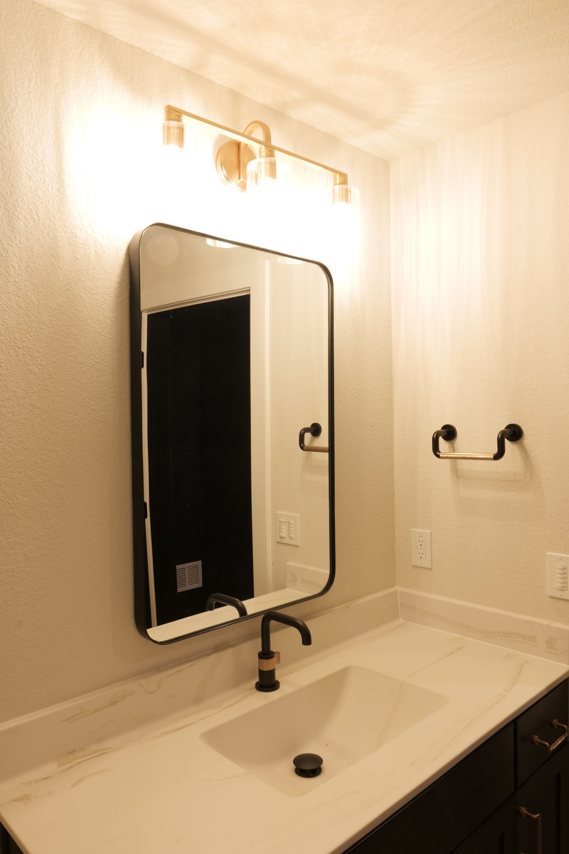 Bathroom with a rectangular mirror, a white countertop, and gold light fixture.