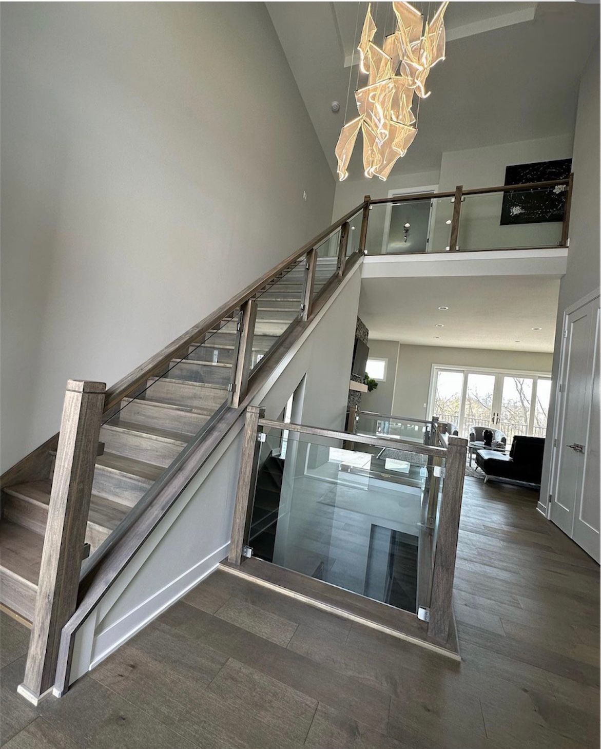 A staircase in a house with a glass railing and a chandelier hanging from the ceiling.