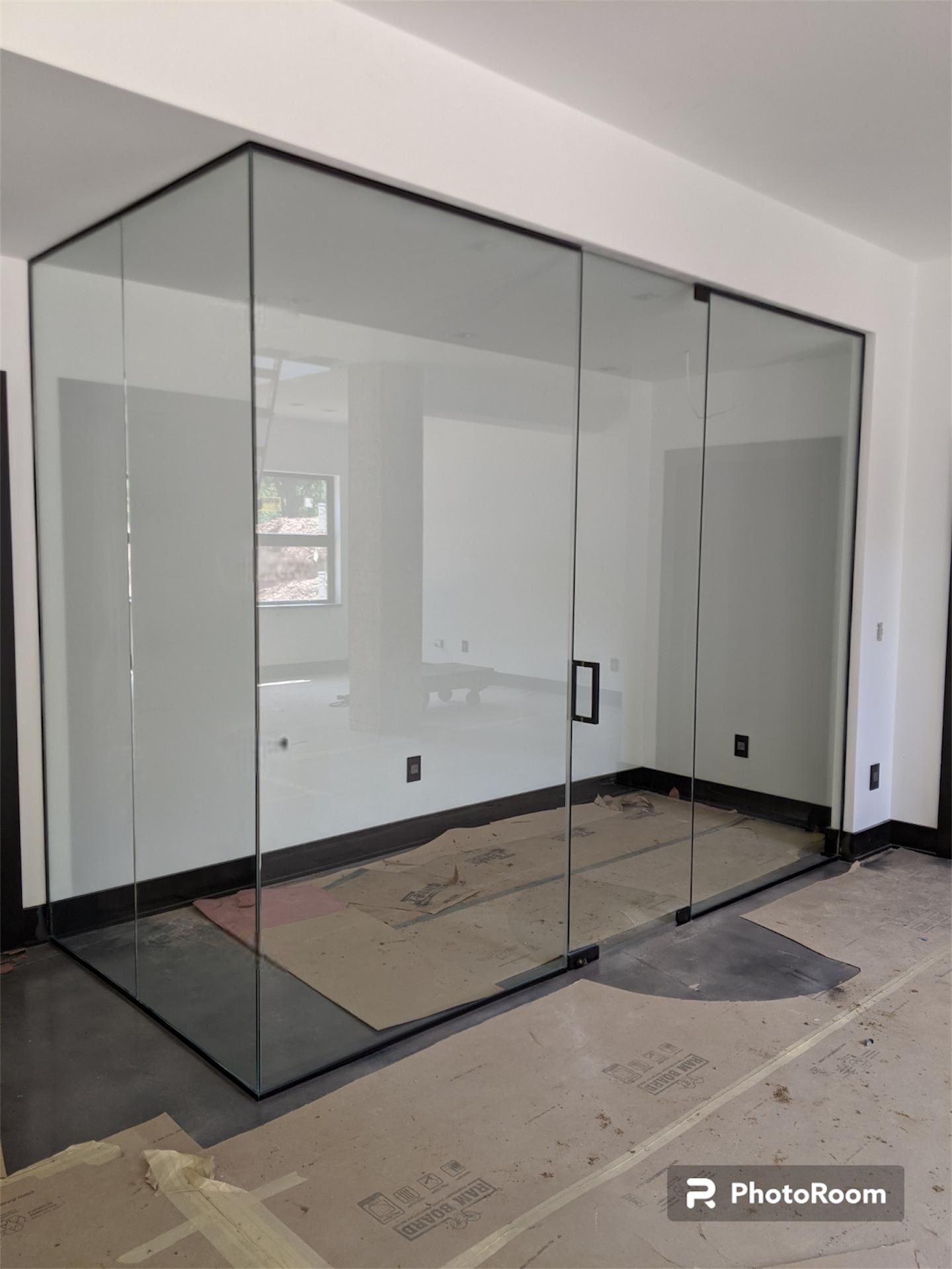 Glass-walled room enclosure with black framing, door, and unfinished interior.