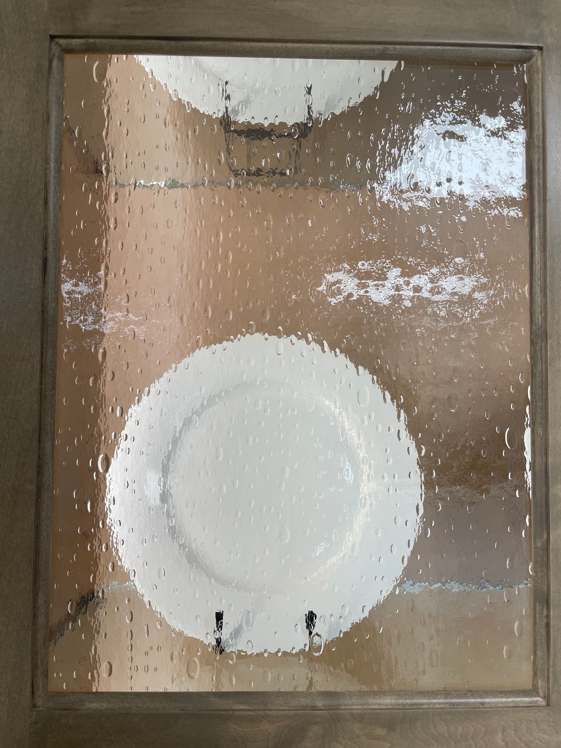 White plates displayed behind textured glass in a wooden cabinet.
