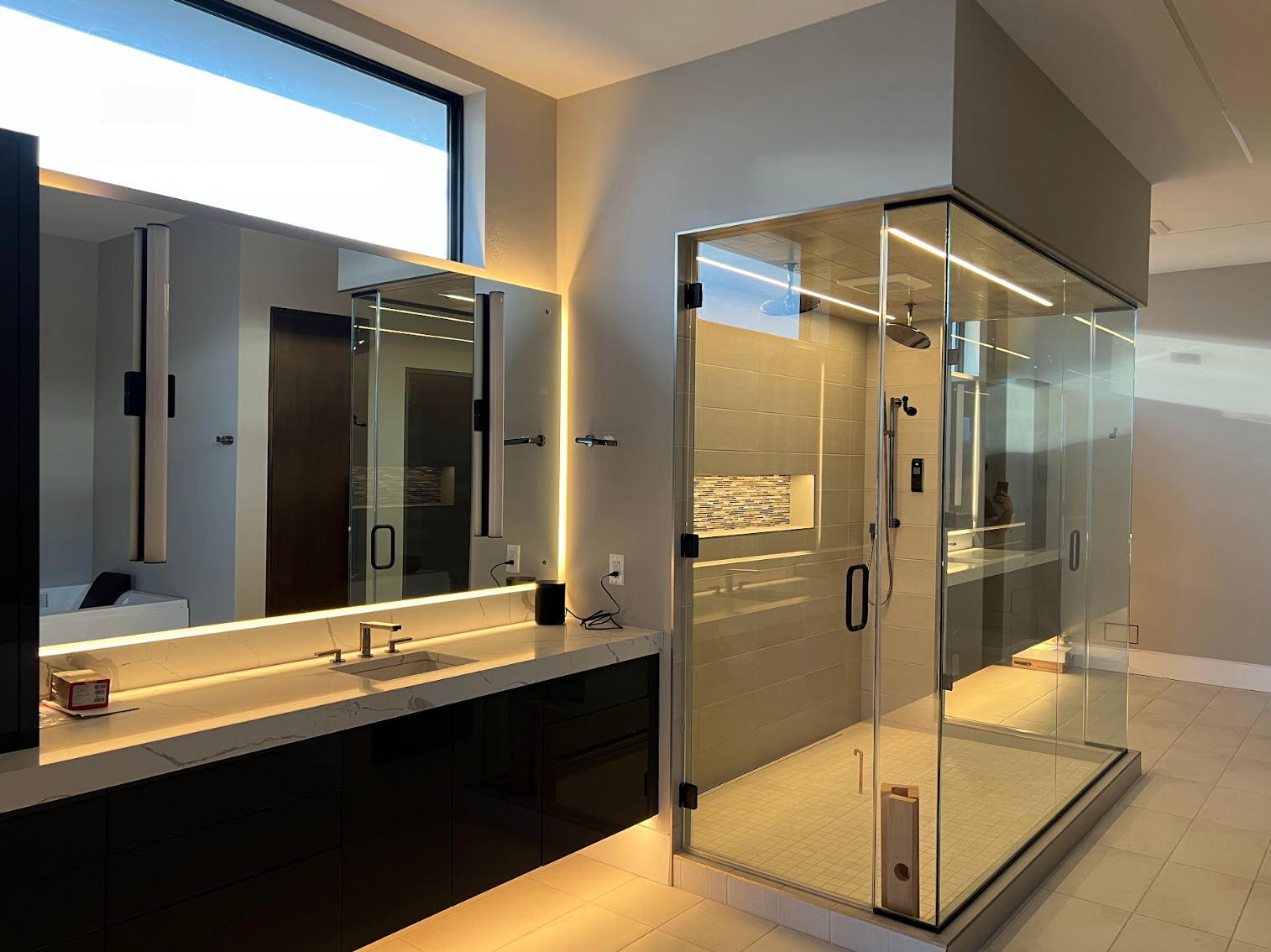 Modern bathroom with glass shower, large mirror, and dark vanity. Bright, neutral colors.