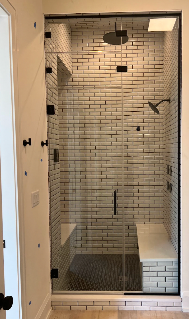 Glass-enclosed shower with white brick tile, black fixtures, and built-in bench.