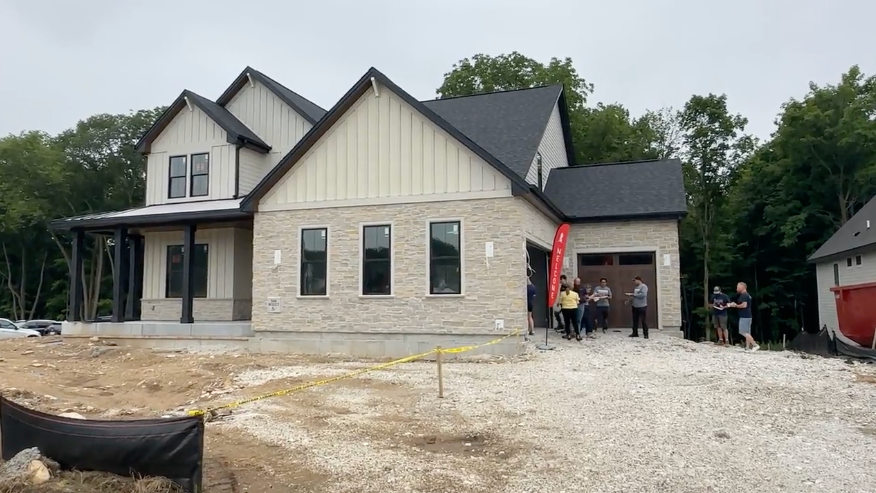 New house under construction; light brick, dark roof; people gathered near garage door.