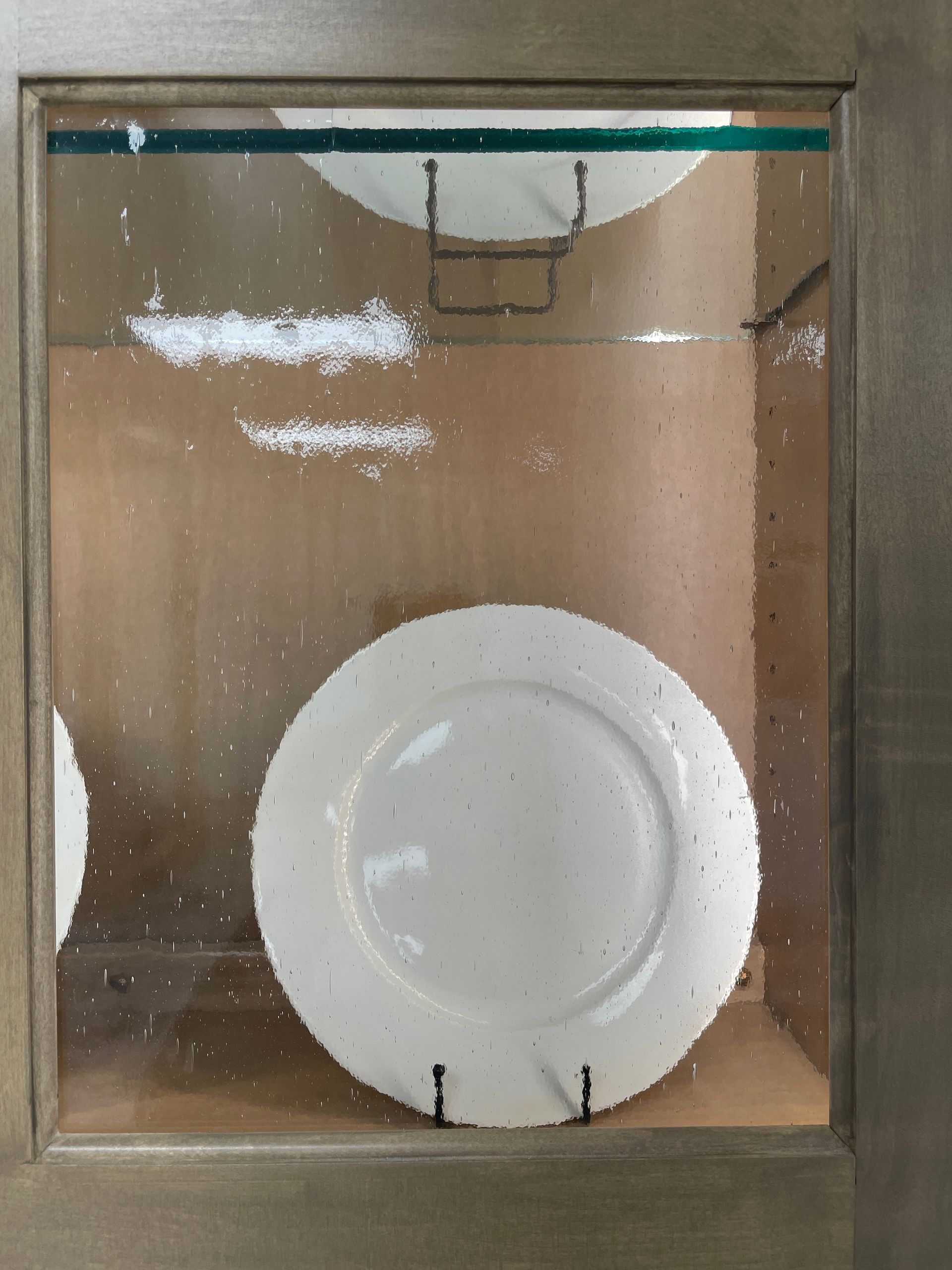 Cabinet with glass door holding white plates on wire plate stands.