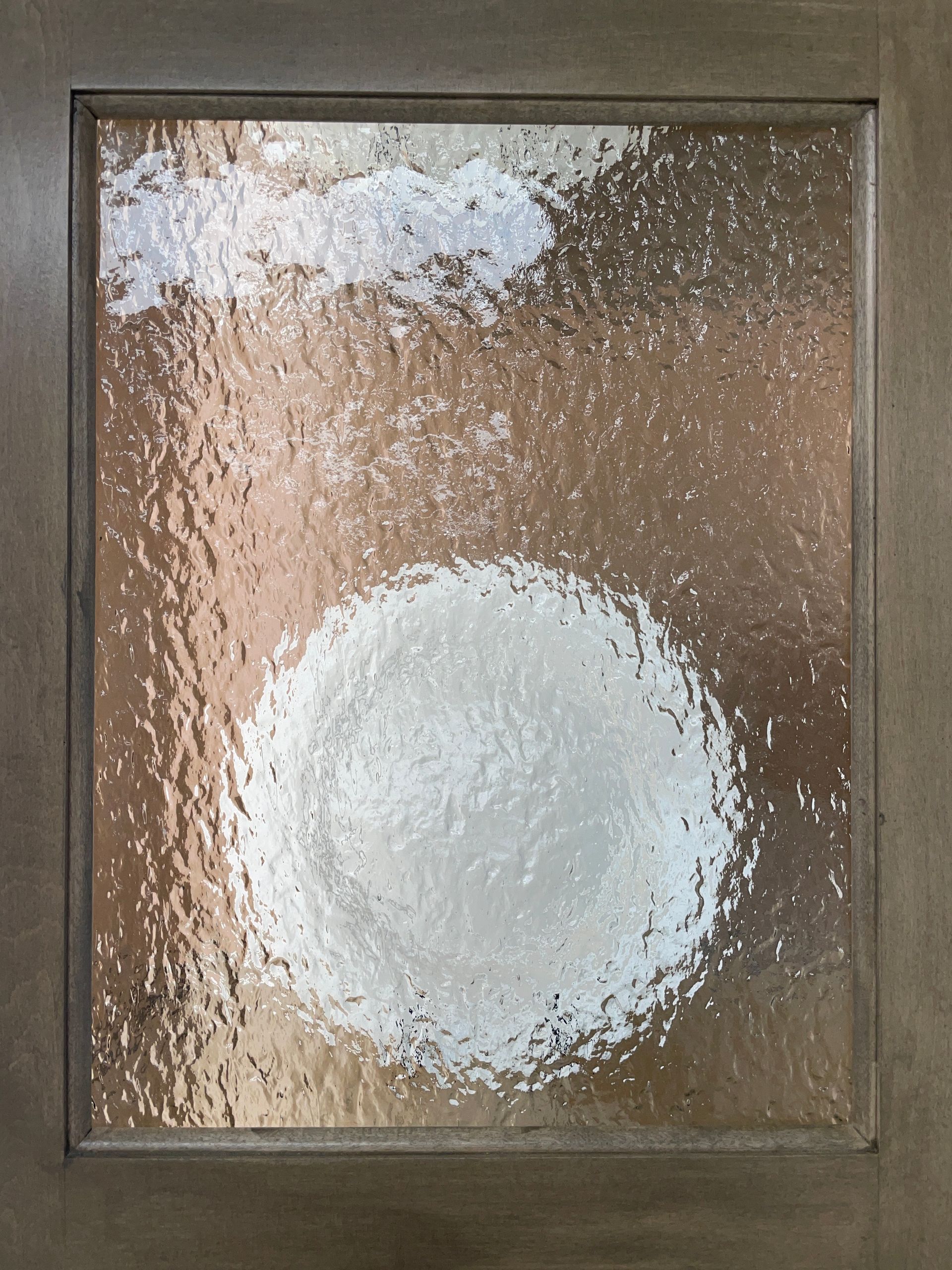 Frosted glass door panel with a bright, circular shape. Soft light is visible behind the glass.