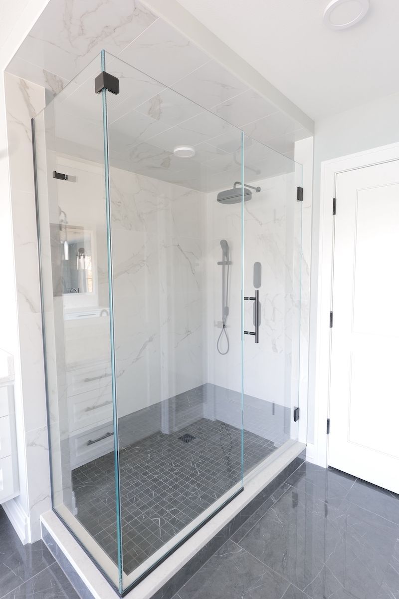 Glass-enclosed shower in a modern bathroom. White marble tile walls, dark floor, and pebble shower base.