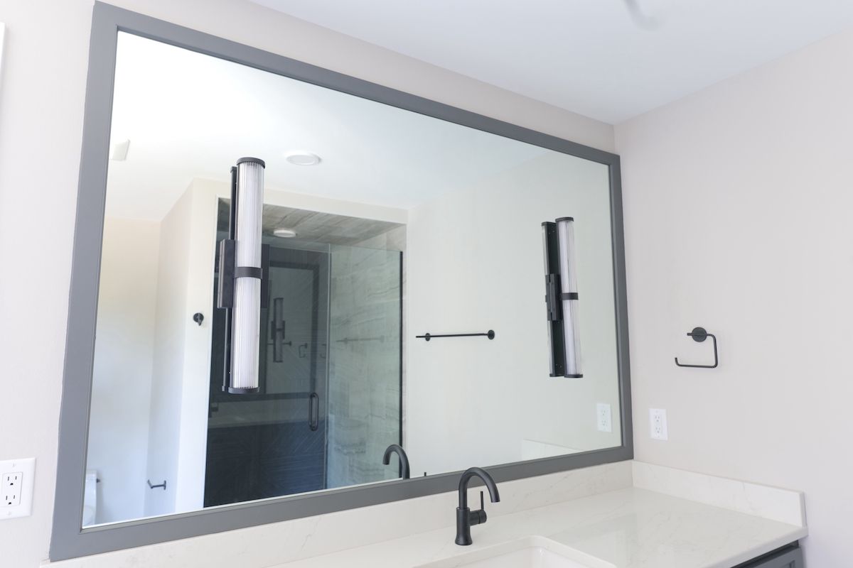 Large rectangular mirror with a gray frame above a white countertop in a bathroom.