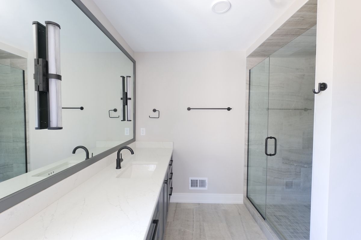 Bathroom with long vanity mirror, glass shower, and gray cabinets.