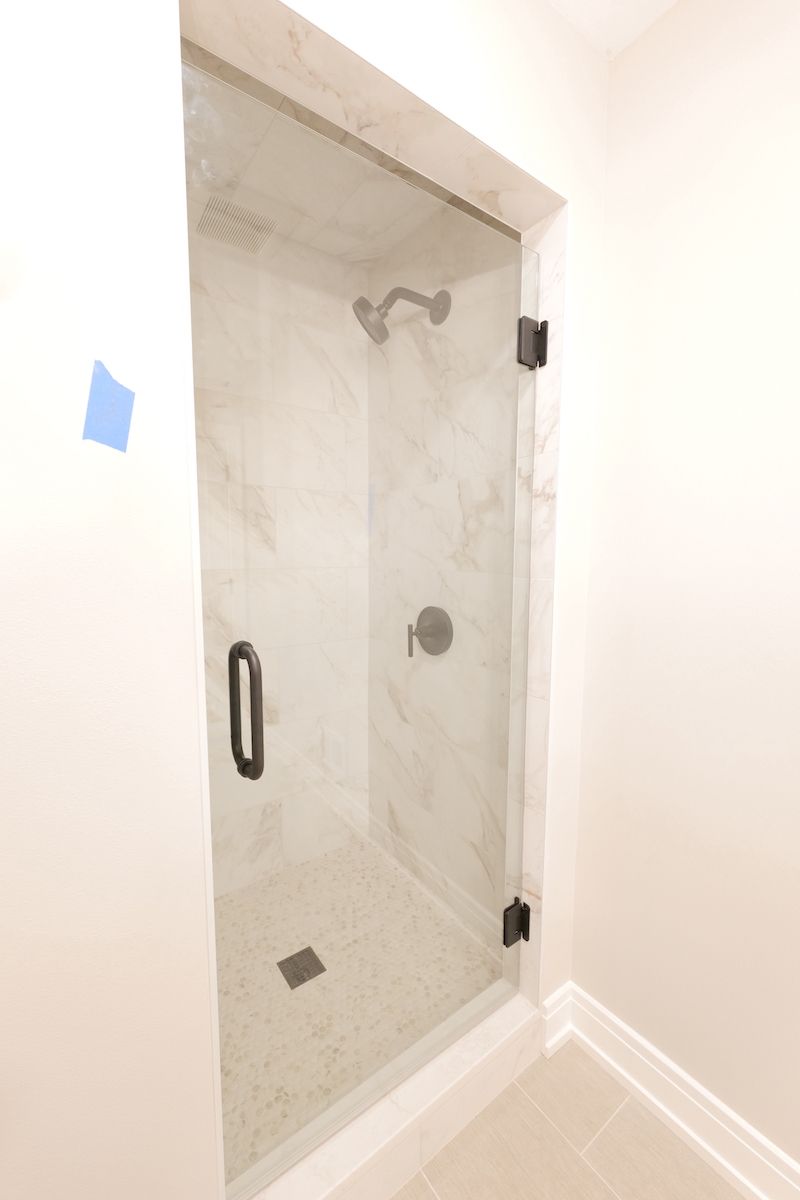 Glass shower enclosure with black hardware, marble-like tile, and silver shower head and controls.