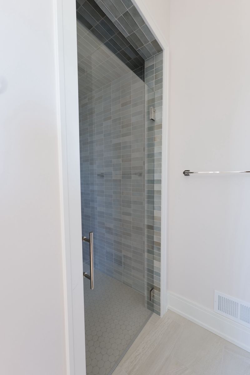 Glass shower with gray tile, open doorway, chrome handle and towel bar.