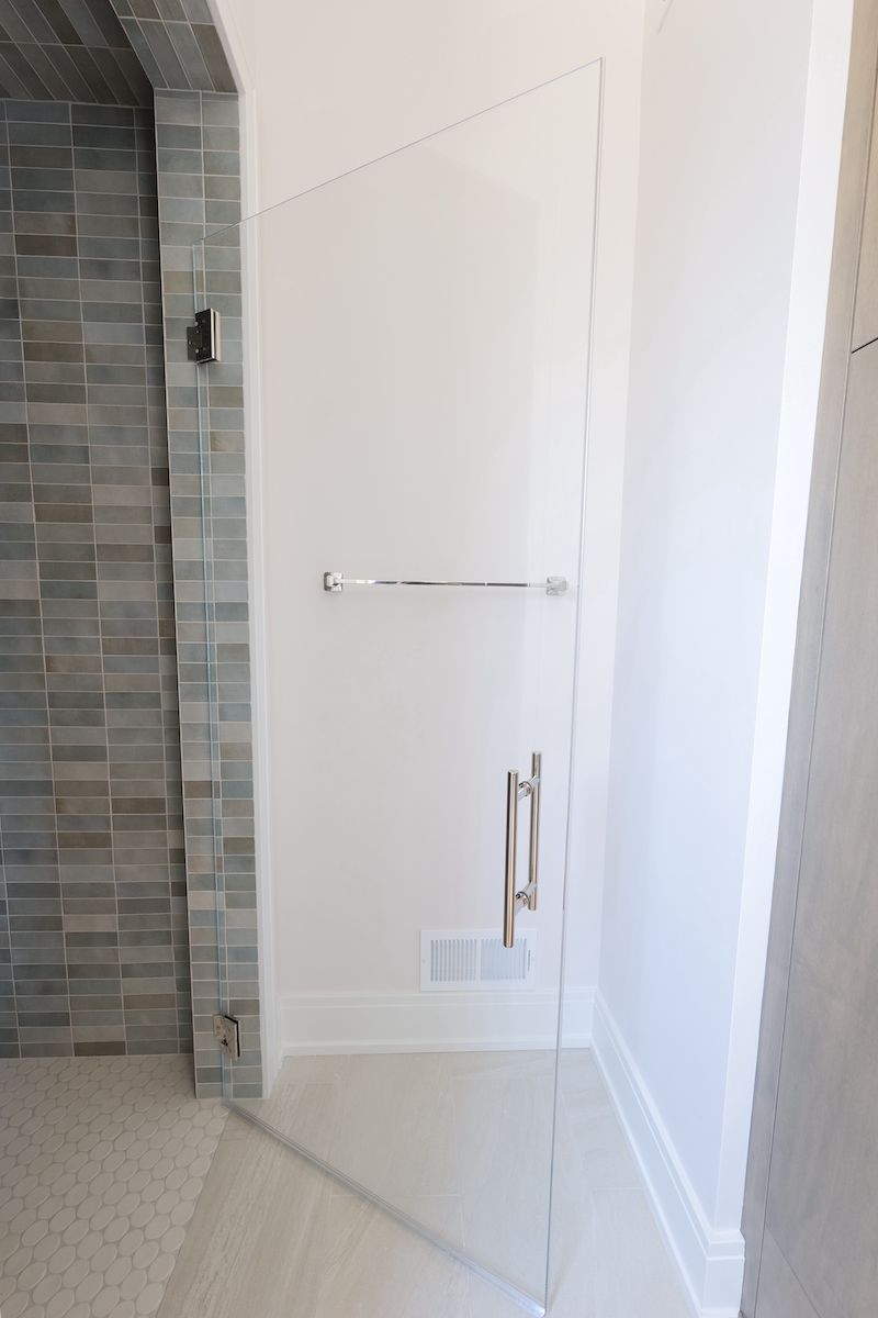 Glass shower door with a towel bar and handle, next to a tiled wall.